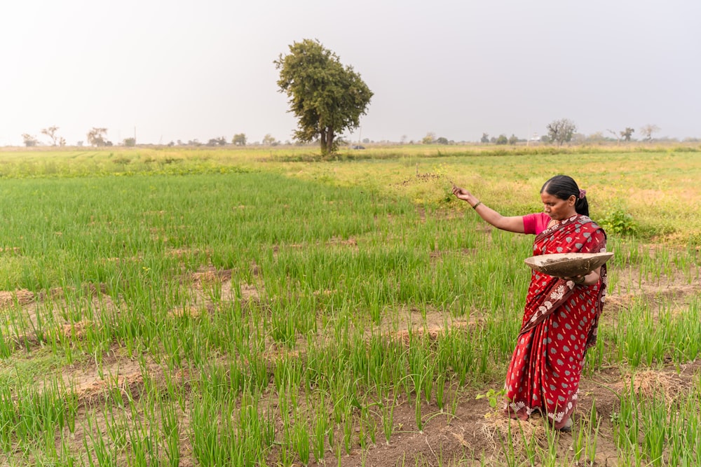 a woman in a red and white sari is standing in a field