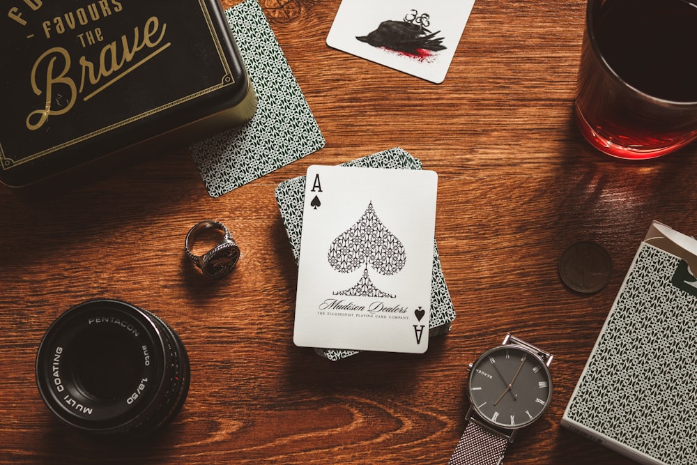 a wooden table topped with playing cards and a watch