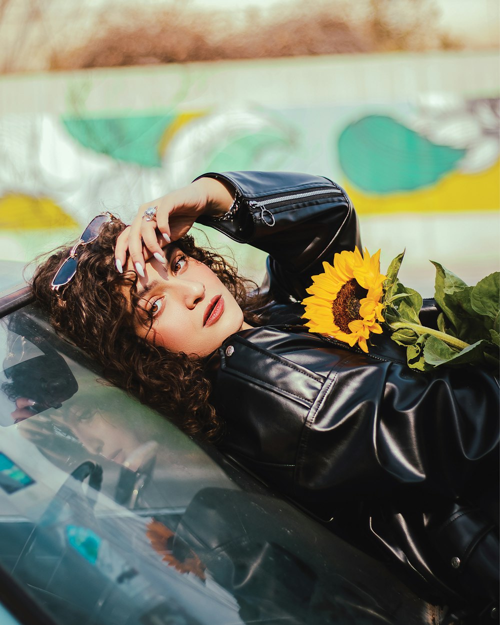 a woman laying on top of a car next to a sunflower