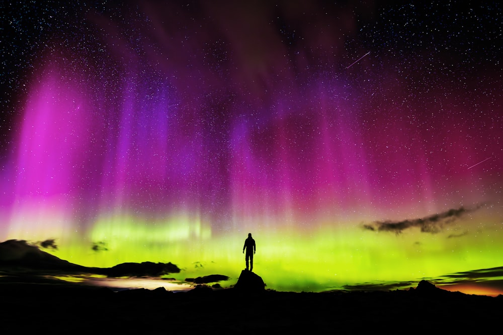 Un hombre parado en la cima de una colina bajo una aurora púrpura y verde