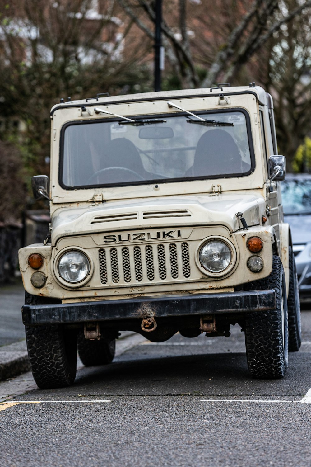 a white jeep driving down a street next to parked cars