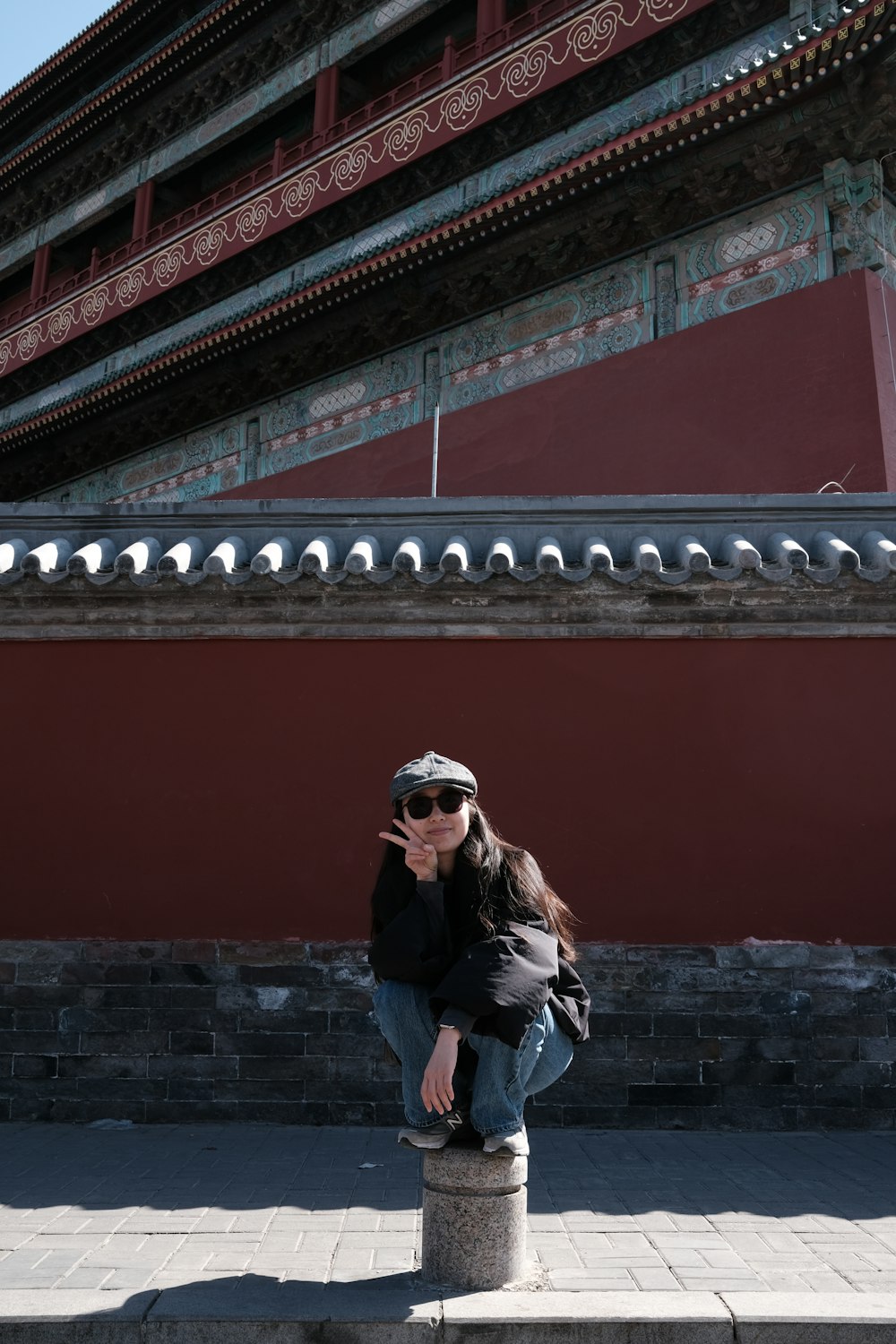 a woman sitting on a pillar in front of a building