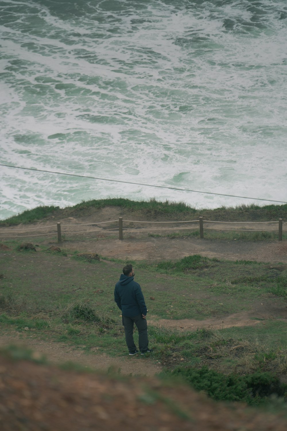 a man standing on top of a lush green hillside next to the ocean