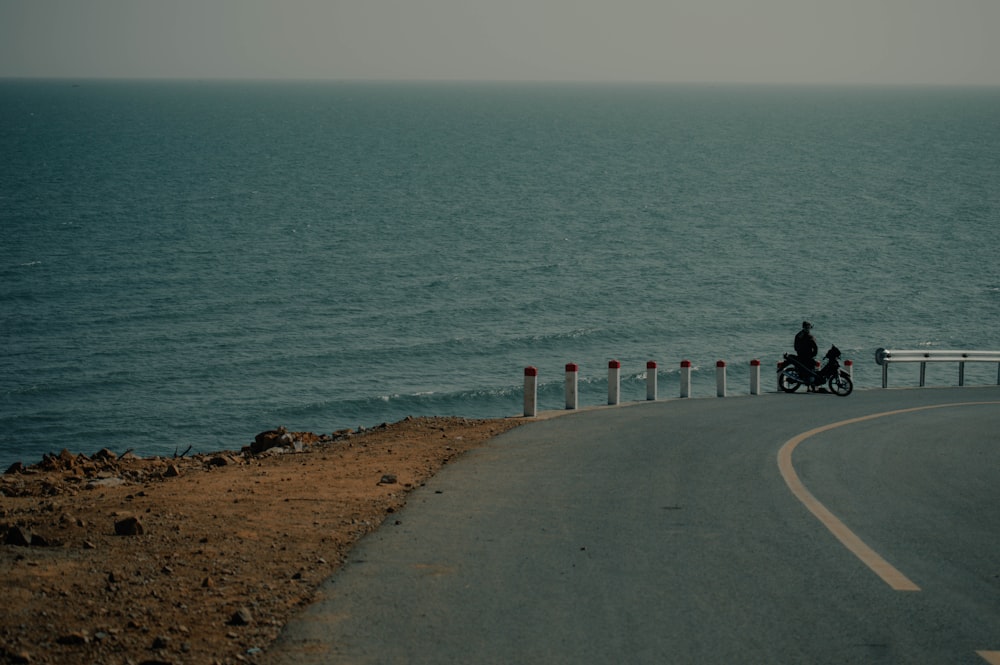 a person riding a motorcycle on a road near the ocean