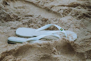 a pair of white flip flops laying in the sand