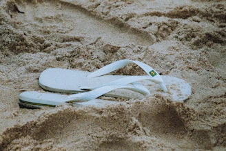 a pair of white flip flops laying in the sand