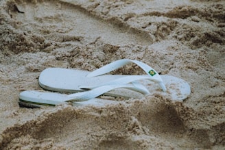 a pair of white flip flops laying in the sand