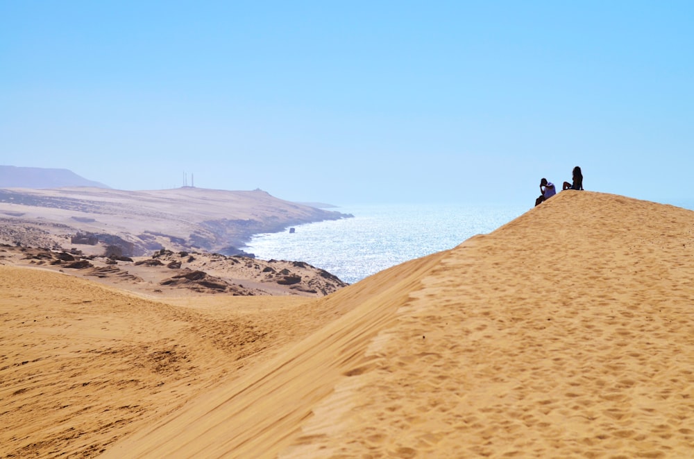 a group of people sitting on top of a sandy hill