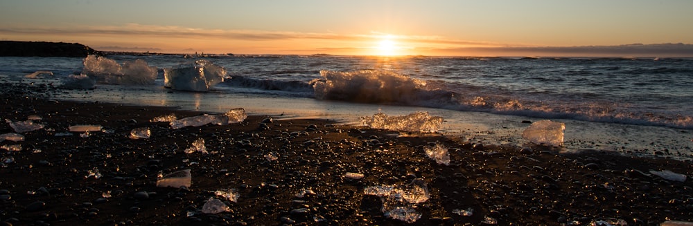 the sun is setting over the ocean with ice chunks on the shore