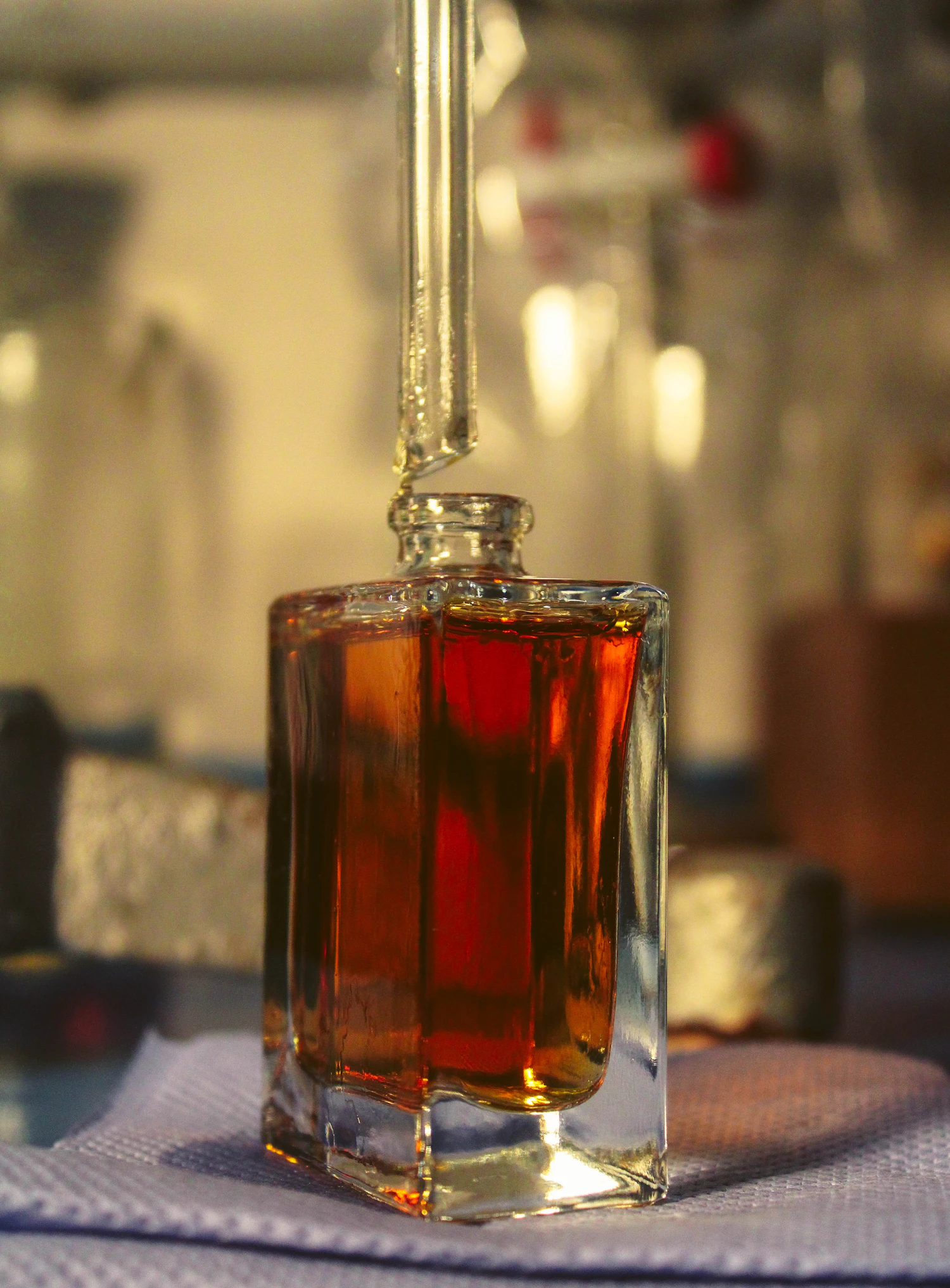 A square flacon filled with dark garnet Rosa d’Ombra, a pipette resting in its neck, on the bench at night