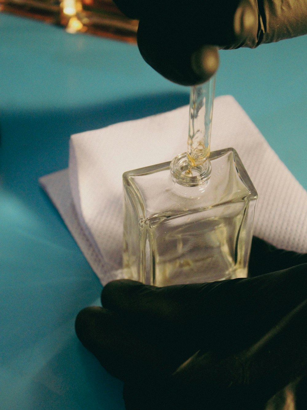 a person in black gloves is putting something in a square glass bottle