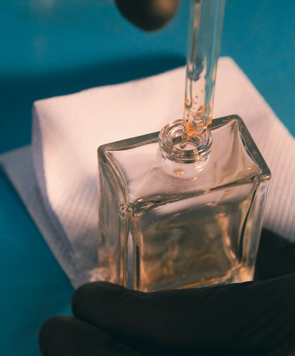 a hand holding a glass bottle with a liquid inside of it