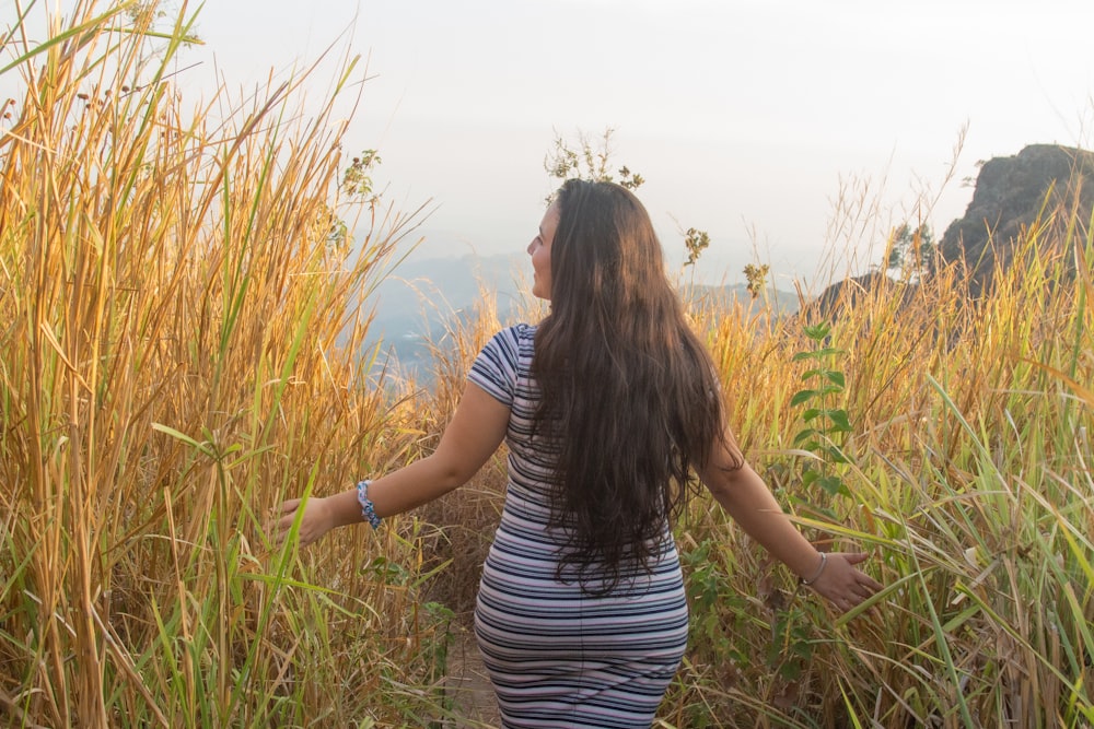 a woman walking through tall grass on top of a hill