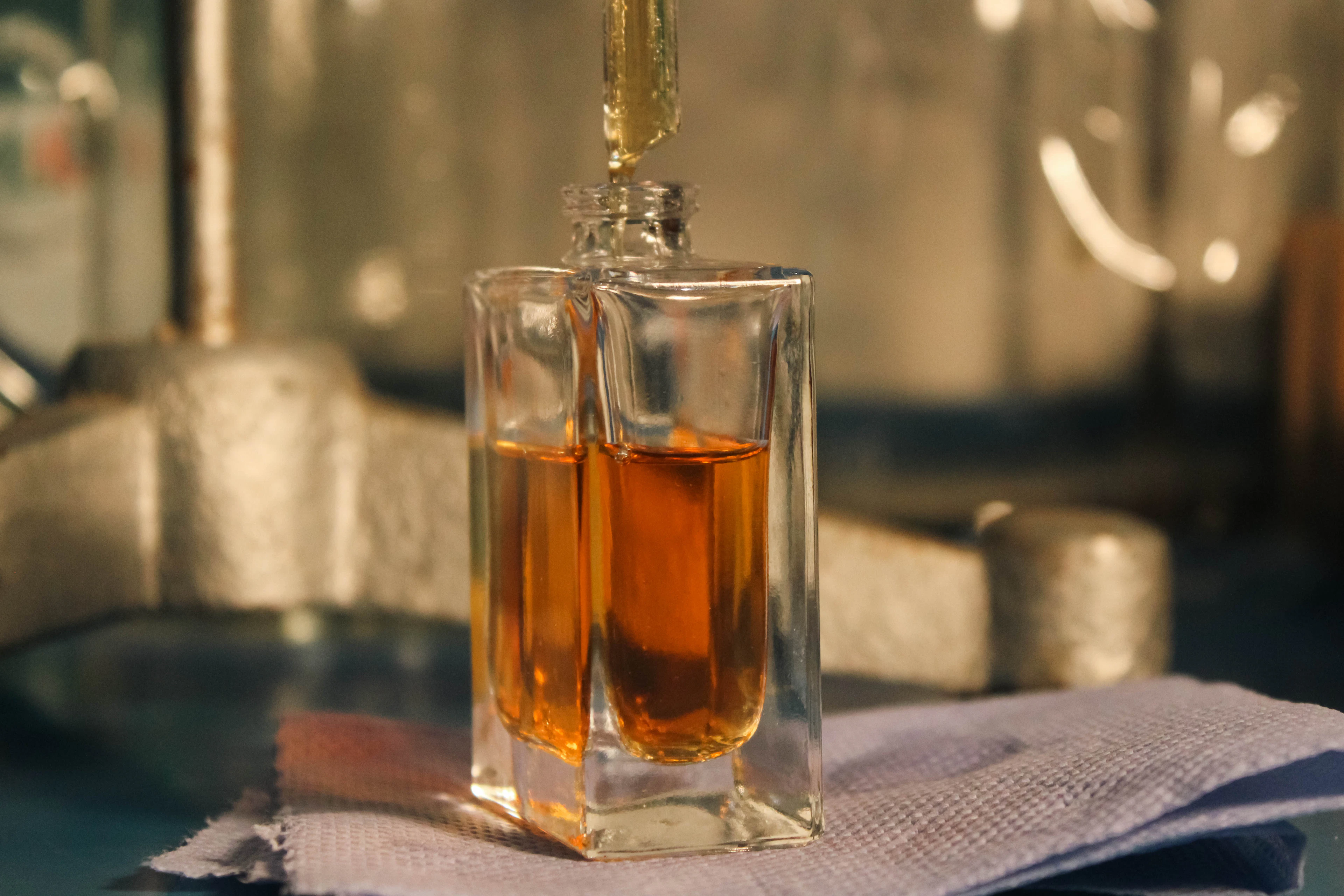 A perfumer's pipette above an amber flacon in the atelier