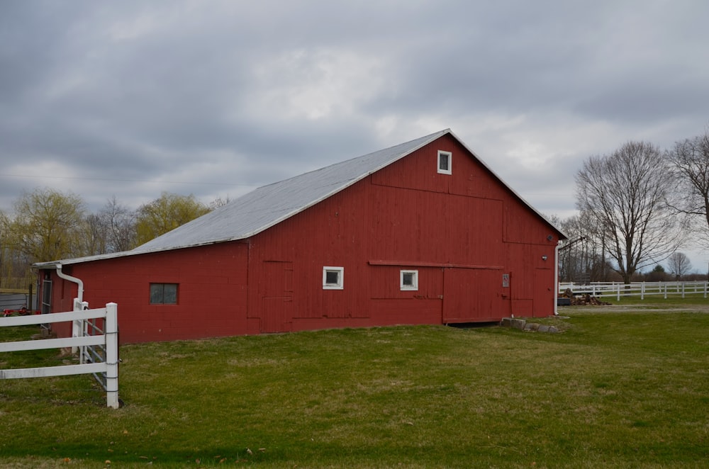 a red barn with a white fence and trees in the background