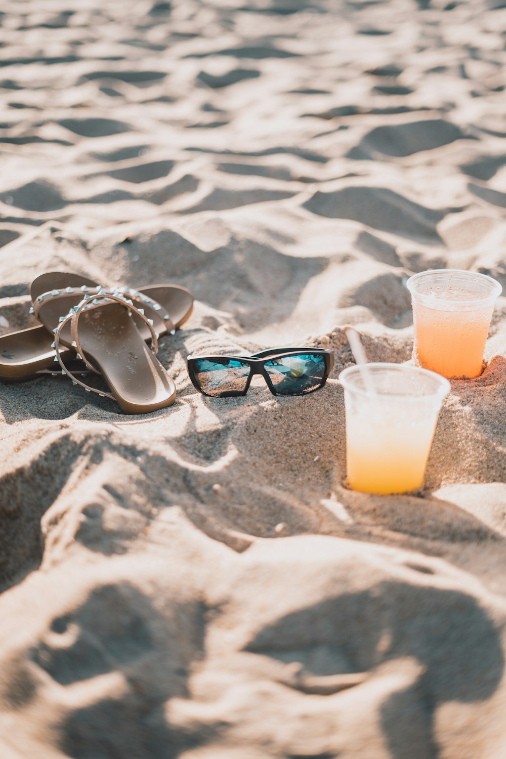 a pair of flip flops, sunglasses, and a drink on a sandy beach