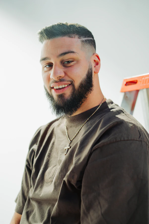 Tyler Brooks, AC Installation Expert at Arctic Air of South Florida — bearded technician in a work T-shirt smiling on a job site beside a step ladder