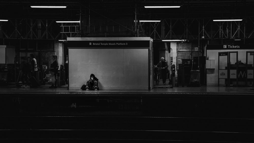 a black and white photo of a person sitting on a train platform