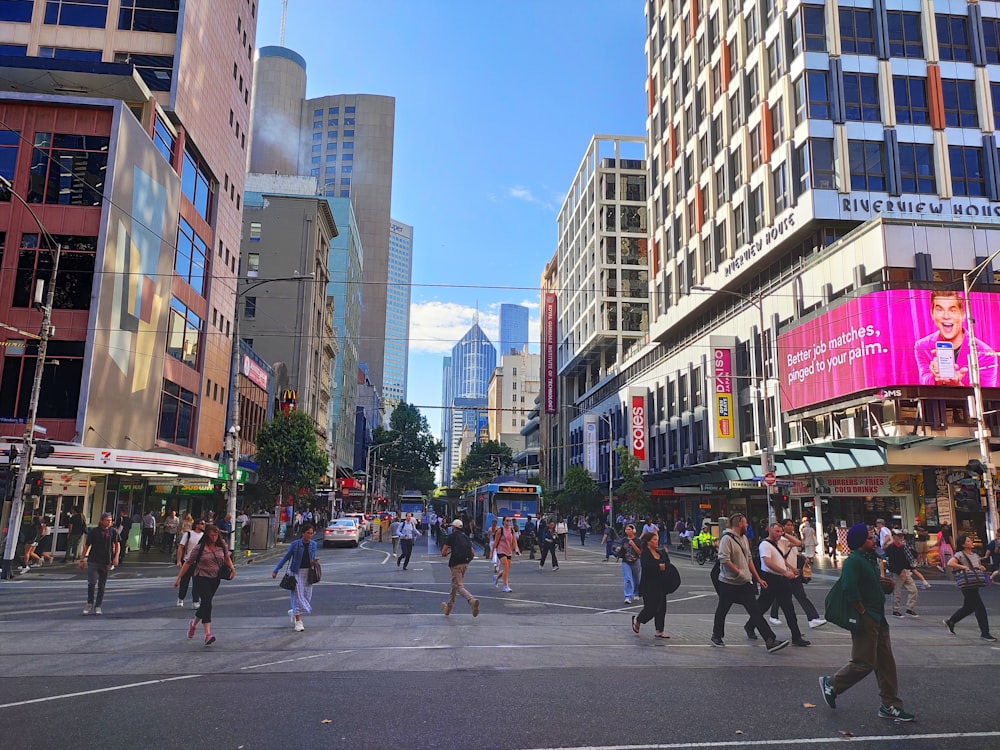 a group of people walking across a street next to tall buildings