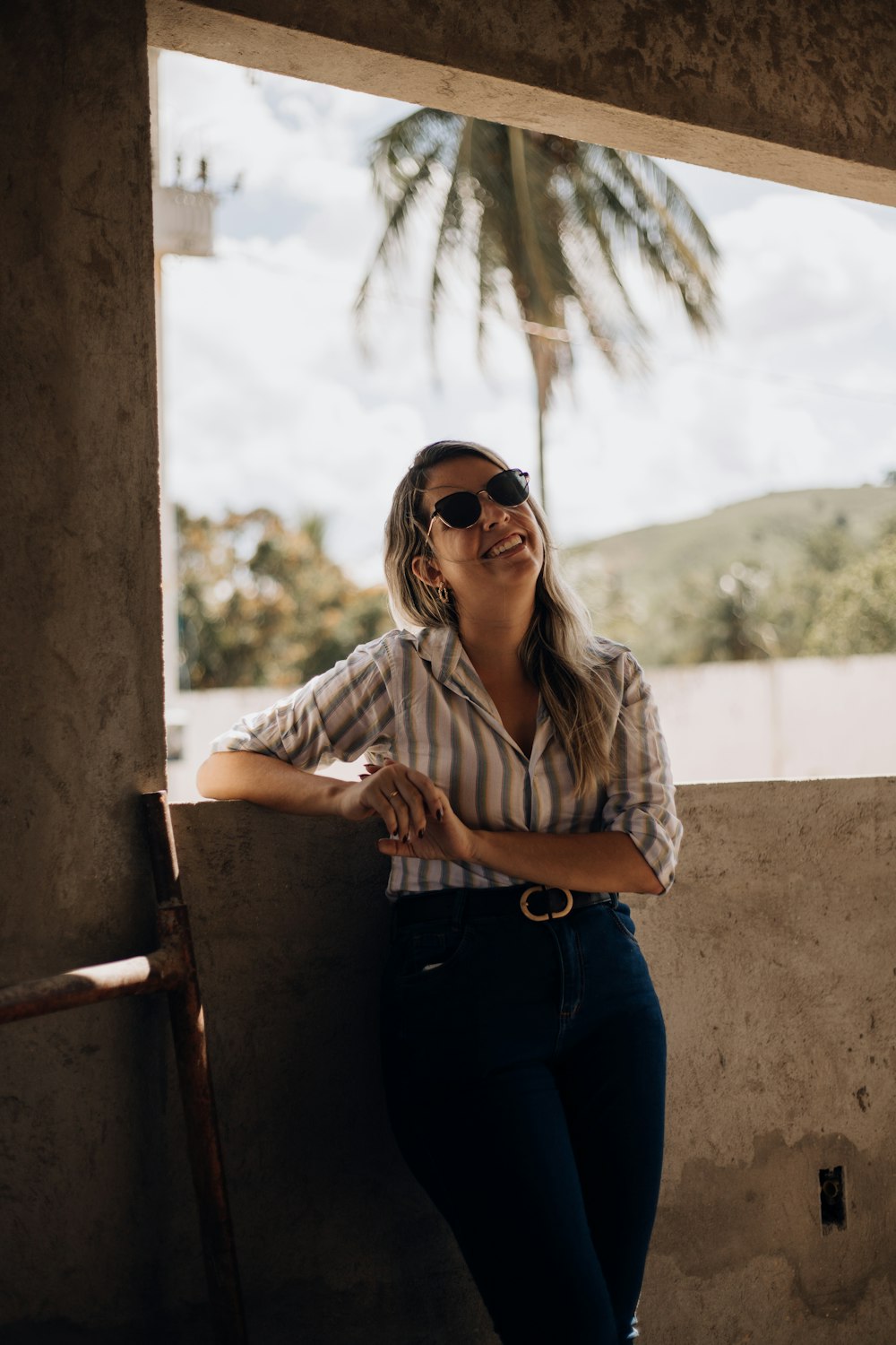 a woman leaning against a wall with a palm tree in the background