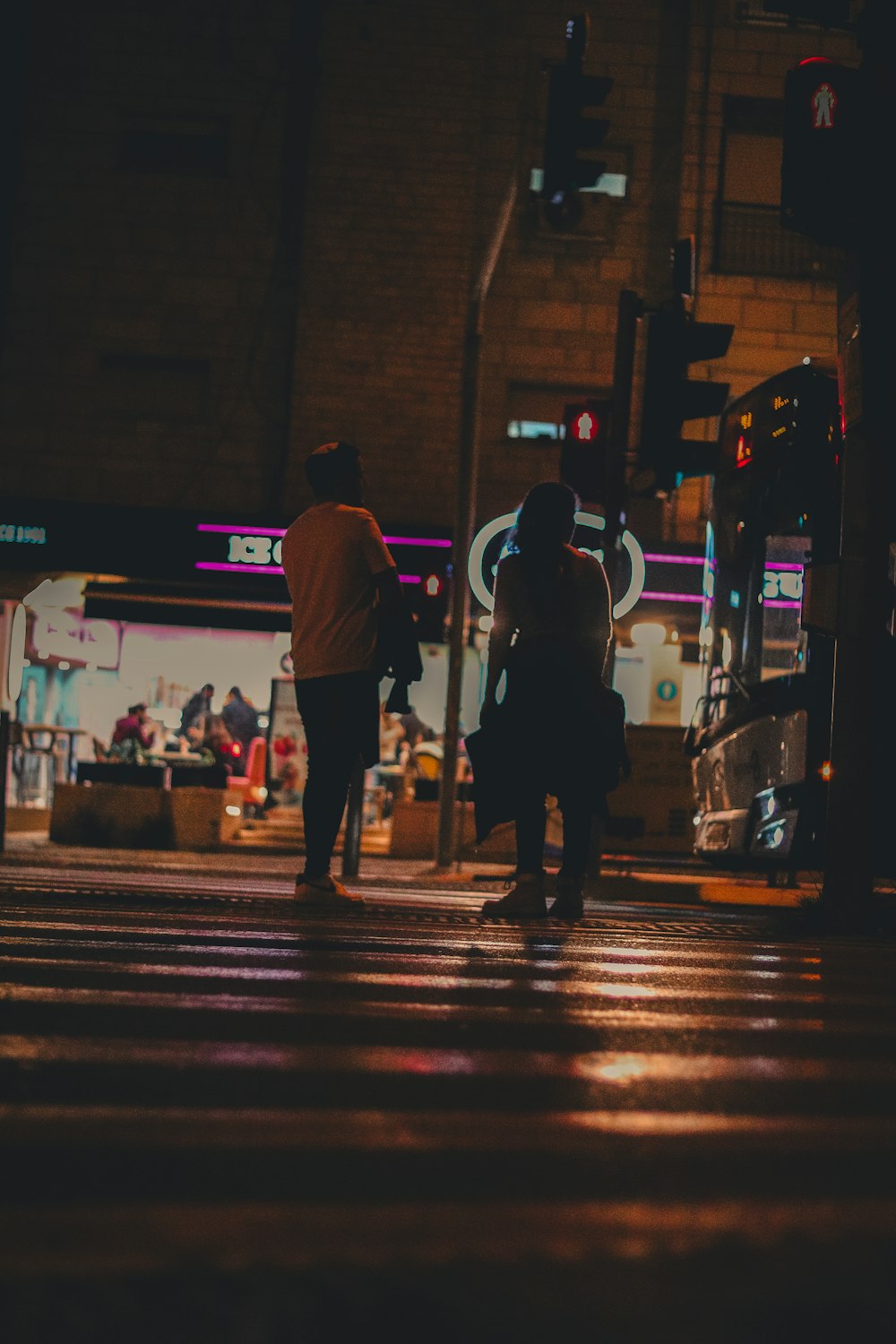 a couple of people walking across a street at night