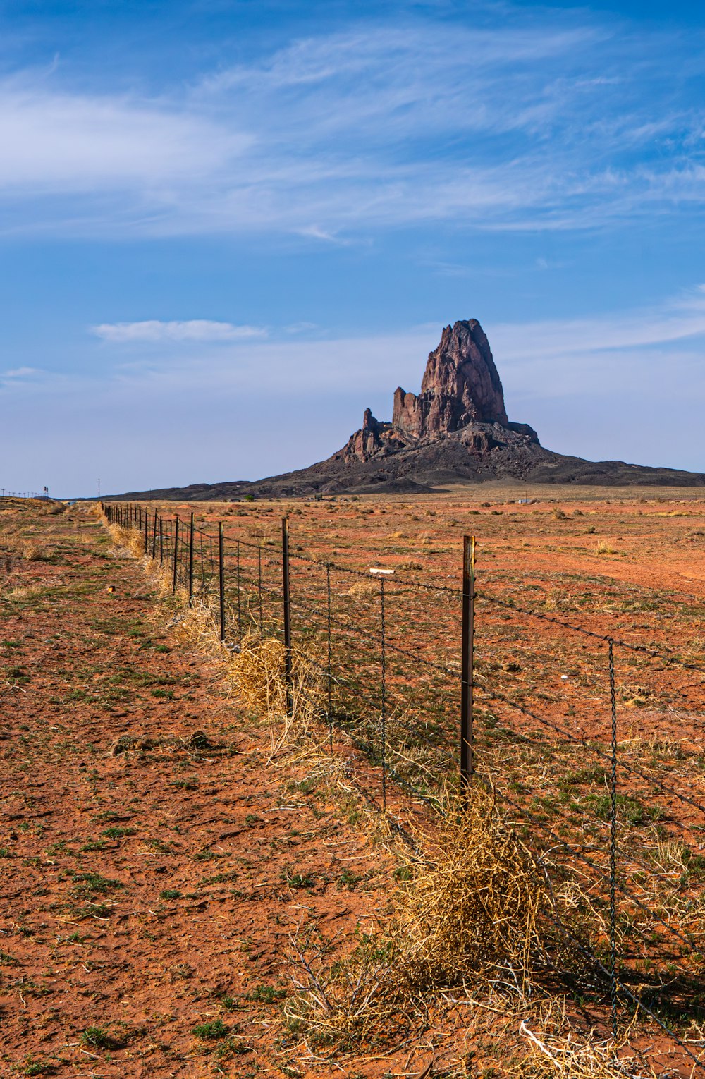 a dirt field with a fence and a mountain in the background