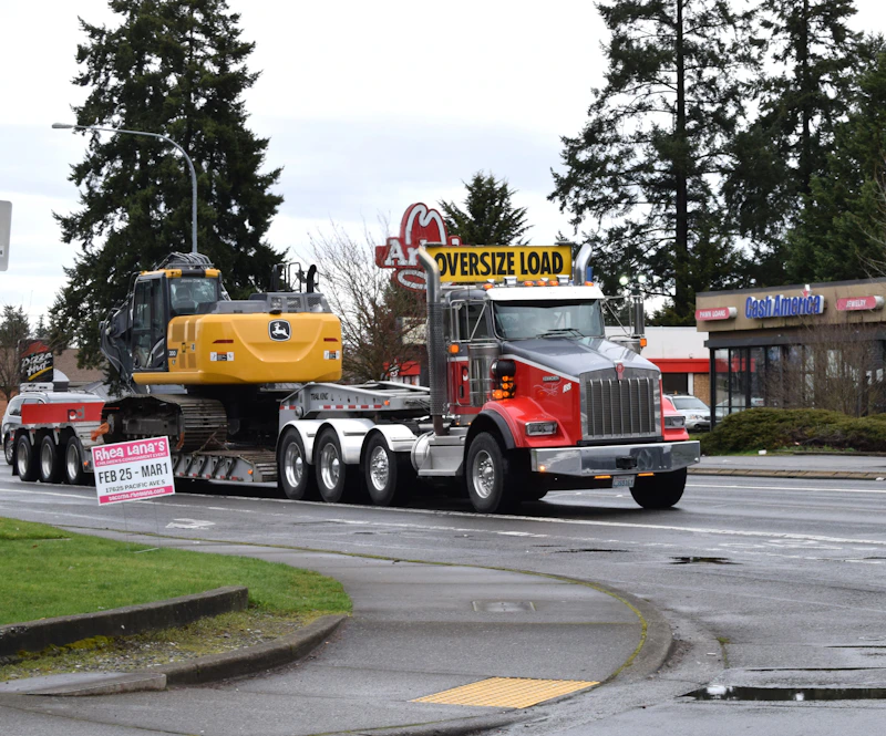 Excavator on a multi-axle lowboy trailer behind a heavy haul tractor displaying an oversize load banner