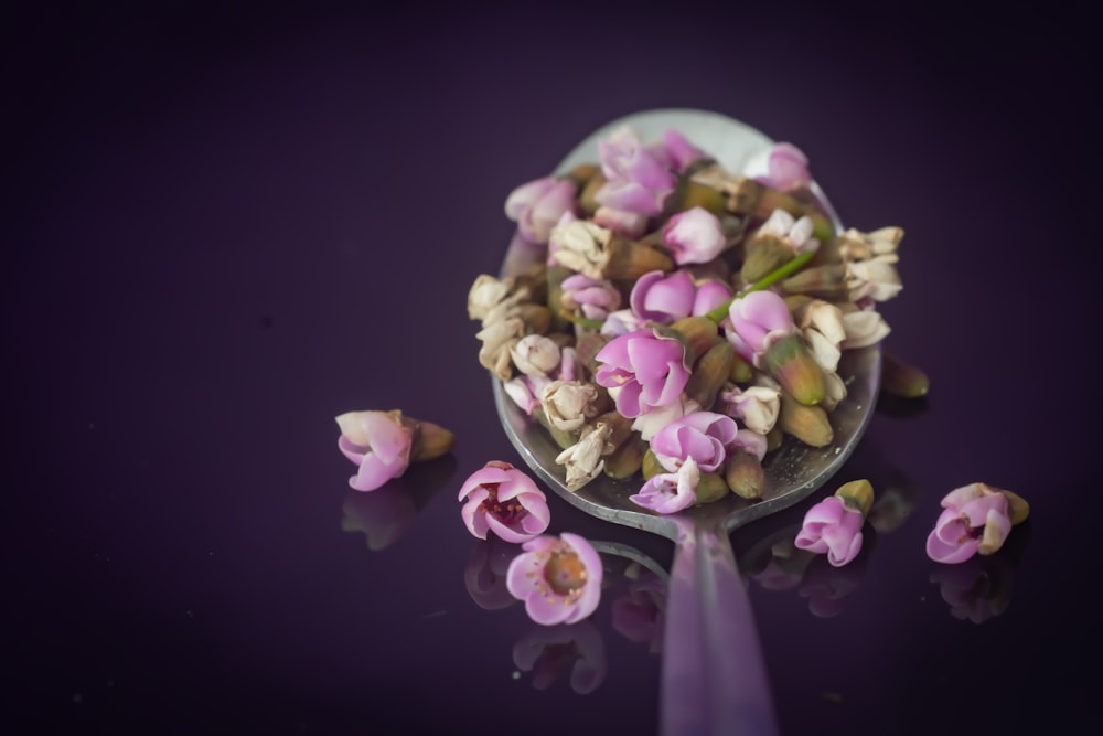 a spoon filled with pink flowers on top of a table
