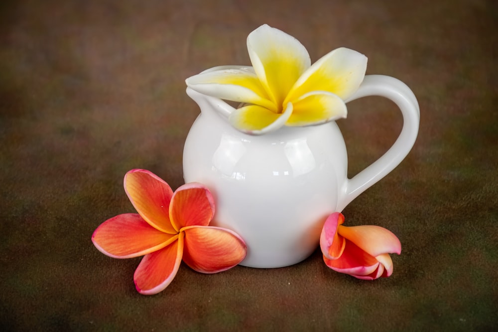 a white pitcher with a yellow and orange flower in it