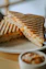 a grilled sandwich on a plate with a bowl of dipping sauce