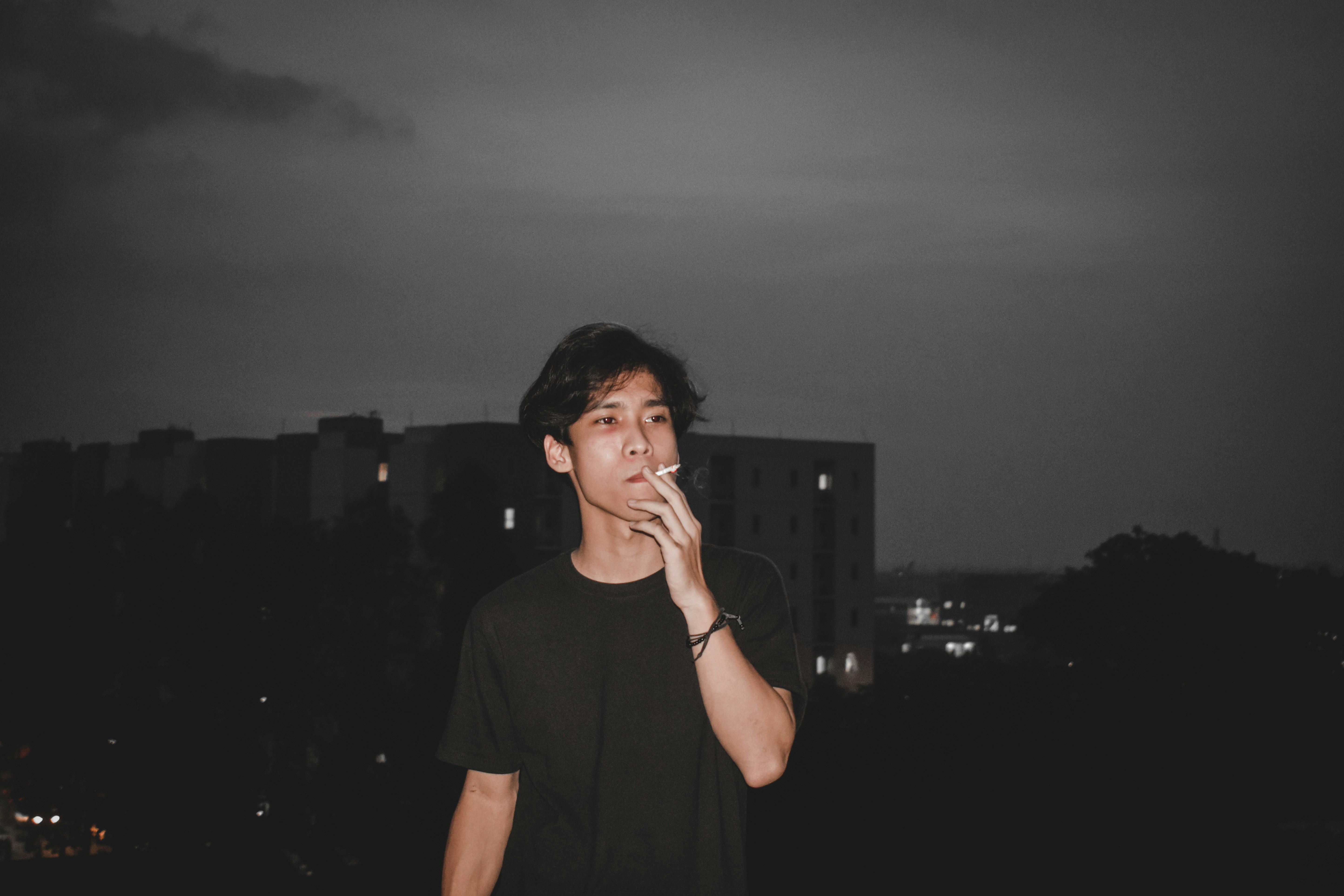 a young man smoking a cigarette in a city at night