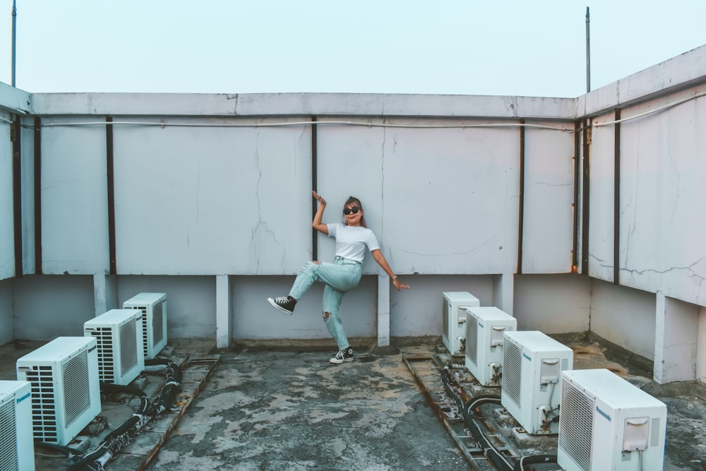 a woman leaning against a wall in front of a bunch of air conditioners
