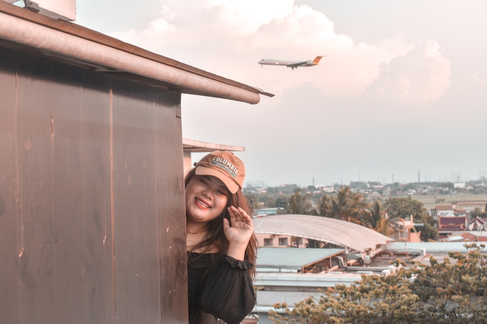 a woman leaning on a building with a plane in the background