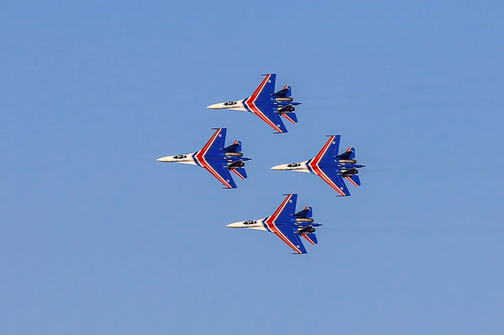 four jets flying in formation in a blue sky