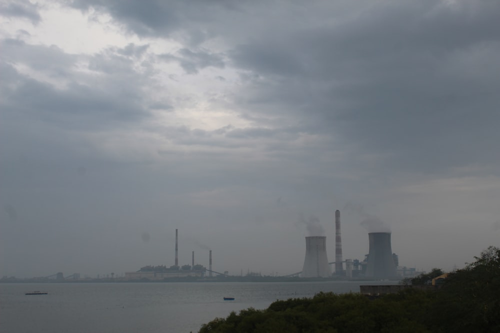 smoke stacks rise from a factory near a body of water