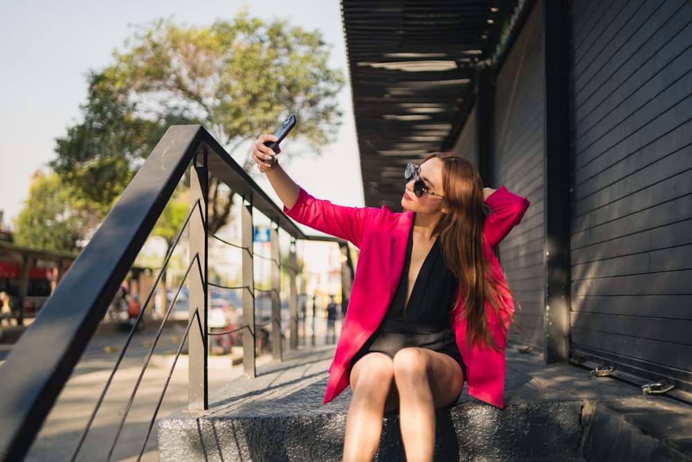 a woman in a pink jacket and black dress sitting on a set of stairs