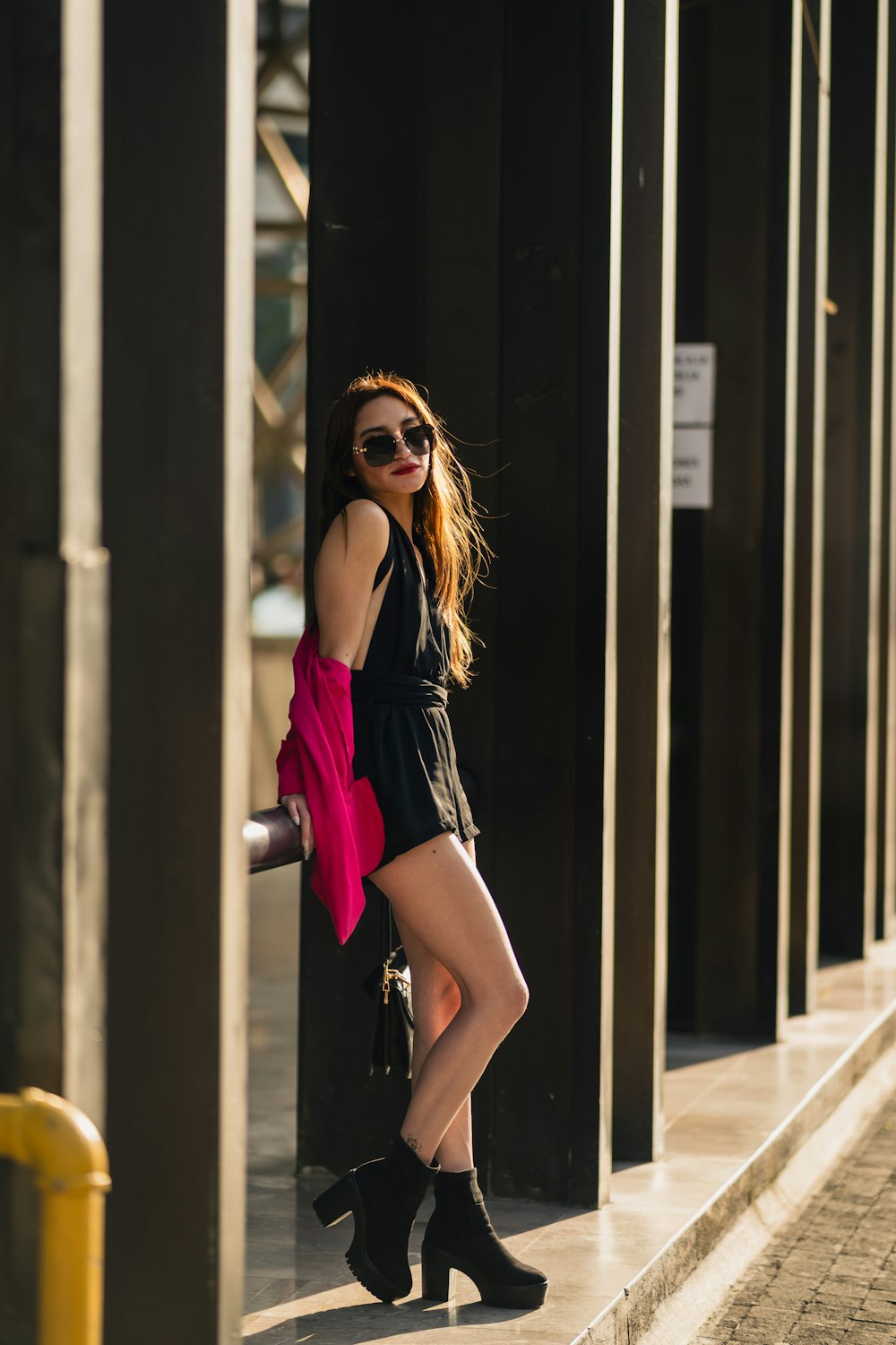 a woman in a short black dress leaning against a wall