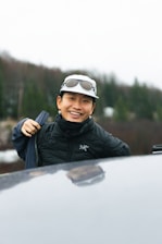 a man wearing a hat and goggles standing next to a car