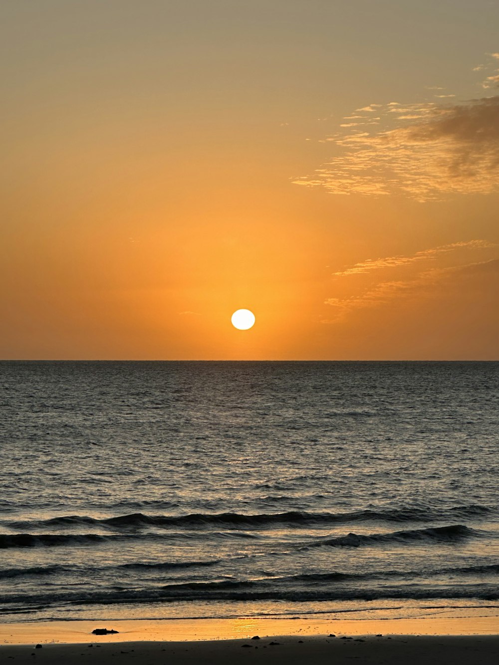 the sun is setting over the ocean on a beach