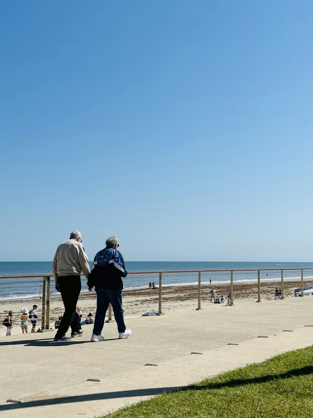 a couple of people walking down a sidewalk near the ocean