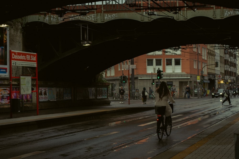 a woman riding a bike down a street under a bridge