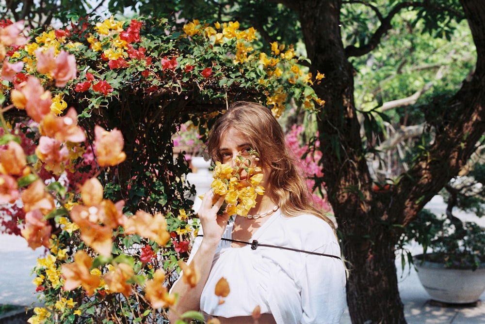 uma mulher em uma camisa branca segurando uma flor amarela e vermelha