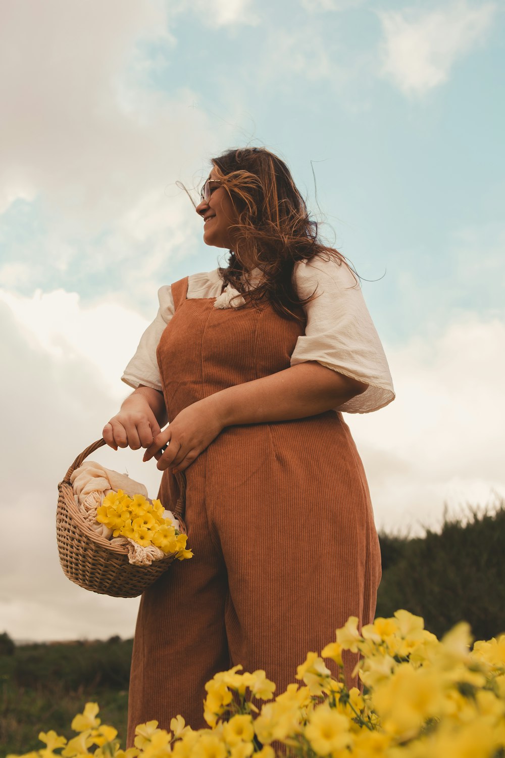 a woman standing in a field holding a basket of flowers