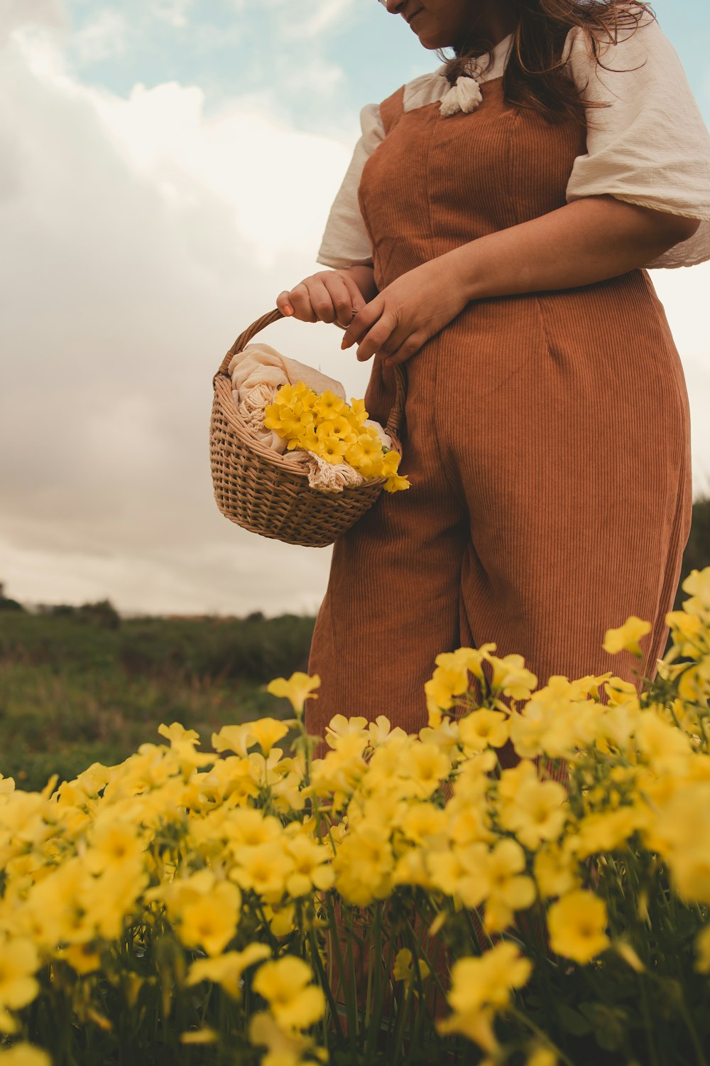 a woman standing in a field holding a basket of flowers