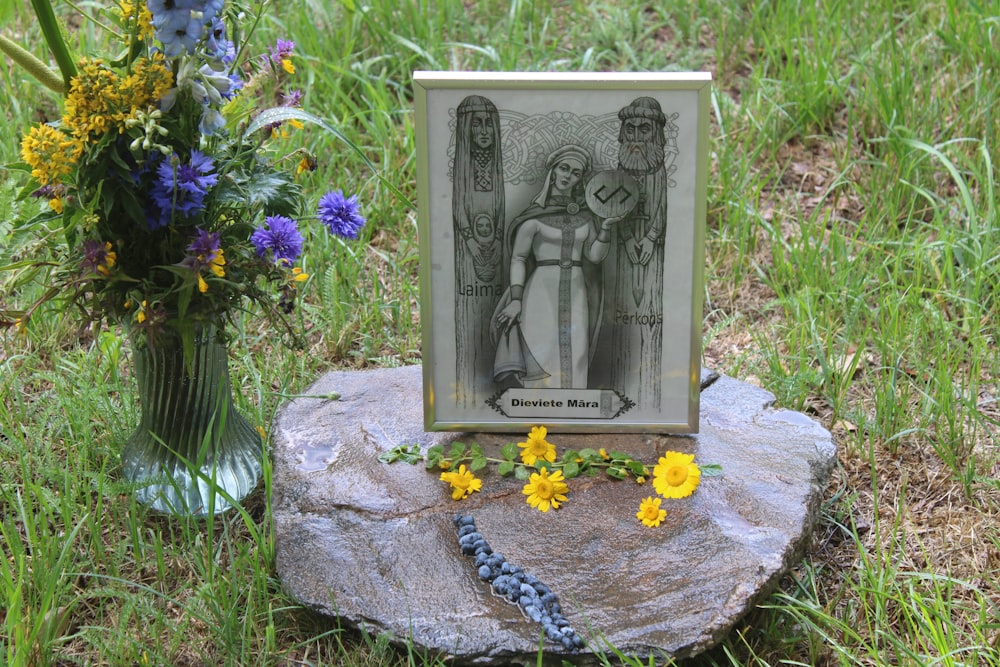 a picture frame sitting on top of a rock next to a vase of flowers