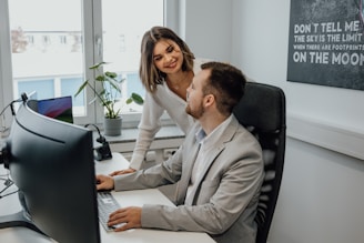 a man and a woman sitting at a desk in front of a computer