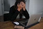 a woman covering her face while looking at a laptop