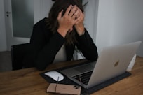 a woman covering her face while looking at a laptop