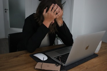 a woman covering her face while looking at a laptop