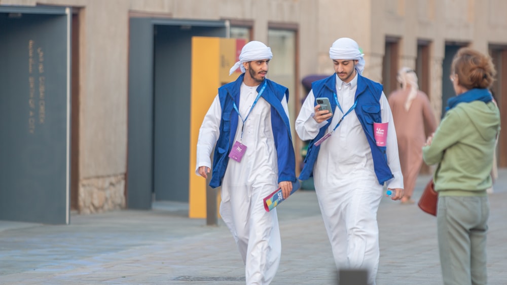 two men dressed in white and blue walking down the street